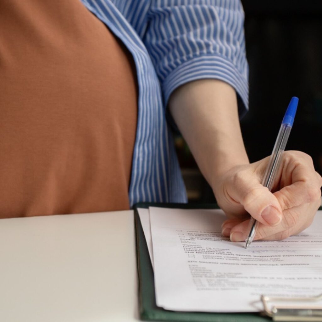 A pregnant woman with a pen in her hand filling out a form.