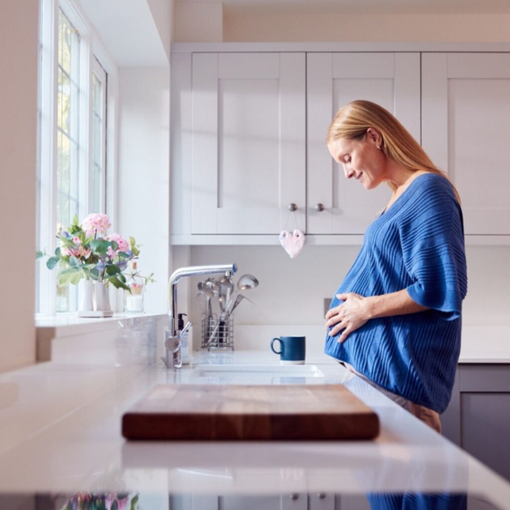 An altruistic surrogate, pregnant standing in a kitchen.